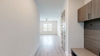 This single-floor space showcases a clean, contemporary design defined by light hardwood-style luxury vinyl plank flooring and bright white walls that run consistently throughout. The open layout is anchored by a living area with a ceiling fan and a window that draws in natural light, creating a welcoming, airy atmosphere.

The kitchen is equipped with stainless steel appliances, including a refrigerator, range, and microwave, paired with dark cabinetry that provides a stylish contrast to the otherwise neutral palette. An adjacent room, accessible through a five-panel interior door, offers flexibility as a dining area or secondary living space with direct sightlines into the kitchen.

Bedrooms are generously proportioned, with large windows fitted with blinds offering outdoor views and ample natural light. Each room features the same consistent flooring and neutral wall tones, contributing to a cohesive aesthetic. Ceiling fans provide additional comfort in the main living and sleeping areas.

The bathroom features a soaking tub surrounded by large-format marble-style tiles in white and grey tones, complemented by matte black fixtures that add a modern, refined touch. Recessed lighting and panel doors complete the well-appointed interior throughout.