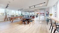This 1060 square foot amenity room in New Westminster, BC, showcases a contemporary and versatile design. The space is characterized by its open floor plan, high ceilings, and abundant natural light streaming through large windows. The room is divided into distinct yet interconnected areas, each serving a specific purpose.

The main living area features a luxurious sectional sofa arranged around a modern coffee table, ideal for casual gatherings. A standout design element is the unique ceiling treatment with suspended geometric shapes, adding visual interest and acoustic benefits. Adjacent to this is an entertainment zone with a large flat-screen TV mounted above a sleek, built-in fireplace, creating a focal point for the room.

A game area is centrally located, featuring a round table suitable for various activities. The space also includes a bar-height counter with seating, perfect for casual dining or as a workstation. Throughout the room, track lighting and modern fixtures provide adjustable illumination options.

The flooring is a warm, light-toned hardwood that unifies the space and contributes to its airy feel. Carefully selected furnishings in neutral tones with pops of color in accessories create a cohesive and inviting atmosphere. The room's layout and amenities make it an ideal space for residents to socialize, relax, or engage in various activities.