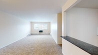 Located at 8053 Lotus Ave in Skokie, IL, this single-floor residence offers a straightforward and functional layout designed for comfortable everyday living. The spacious living area is carpeted in a neutral tone and features large windows that allow natural light to fill the room, creating a bright and open atmosphere. A half-wall with a dark granite countertop separates the living space from the kitchen, providing a convenient pass-through that enhances the open feel of the layout. Built-in shelving near the entryway offers practical storage directly upon entry.

The kitchen is well-appointed with warm wood cabinetry, dark granite countertops, a tile mosaic backsplash, and stainless steel appliances including a gas range, over-the-range microwave, and refrigerator. Light tile flooring completes the space.

The bedrooms are carpeted and finished in soft, neutral tones, each equipped with baseboard heating. One bedroom includes a wall-mounted HVAC unit and a window with exterior views. The bathroom features white subway tile surrounding the tub-shower combination, mosaic floor tile, a white vanity with mirrored medicine cabinet, and chrome fixtures, presenting a clean and classic finish throughout.
