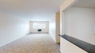 Located at 8053 Lotus Ave in Skokie, IL, this single-floor residence offers a straightforward and functional layout designed for comfortable everyday living. The spacious living area is carpeted in a neutral tone and features large windows that allow natural light to fill the room, creating a bright and open atmosphere. A half-wall with a dark granite countertop separates the living space from the kitchen, providing a convenient pass-through that enhances the open feel of the layout. Built-in shelving near the entryway offers practical storage directly upon entry.

The kitchen is well-appointed with warm wood cabinetry, dark granite countertops, a tile mosaic backsplash, and stainless steel appliances including a gas range, over-the-range microwave, and refrigerator. Light tile flooring completes the space.

The bedrooms are carpeted and finished in soft, neutral tones, each equipped with baseboard heating. One bedroom includes a wall-mounted HVAC unit and a window with exterior views. The bathroom features white subway tile surrounding the tub-shower combination, mosaic floor tile, a white vanity with mirrored medicine cabinet, and chrome fixtures, presenting a clean and classic finish throughout.