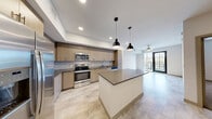 Located at 1050 Blanche St in West Palm Beach, Florida, this modern one-bedroom, one-bathroom residence offers a thoughtfully designed single-floor layout. The open-concept kitchen and dining area serves as the heart of the home, showcasing light wood-grain cabinetry, a grey subway tile backsplash, stainless steel appliances including a refrigerator, range, microwave, and dishwasher, and a large central island with a dark quartz countertop. Stylish pendant lights hang above the island, complementing the recessed lighting throughout. Light-toned tile flooring flows through the main living areas, adding a clean, contemporary feel. The living room connects seamlessly to a private balcony through glass-paneled doors, offering outdoor views of the surrounding West Palm Beach neighborhood framed by tropical palm foliage. The bedroom features soft carpeting, a ceiling fan, and a bright window that invites natural light. Generous closet space is provided across three closets, including a walk-in with wire shelving. Additional conveniences include an in-unit laundry area. The overall ambiance is clean, modern, and move-in ready, reflecting a contemporary Florida aesthetic.