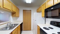 Located at 4111 Wincove Dr in Groveport, Ohio, this single-floor residence offers a practical and well-organized layout designed for comfortable everyday living. The kitchen is a standout feature, designed in a classic galley configuration that maximizes efficiency. It is equipped with warm honey-toned oak cabinetry on both sides, providing generous storage space both above and below the countertops. The kitchen includes a full suite of appliances, among them a white refrigerator, an electric coil cooktop range, a dishwasher, and an over-the-range microwave. Light-toned countertops complement the cabinetry, and a stainless steel sink is conveniently positioned along one wall. The space is illuminated by a flush-mount overhead light fixture, keeping the kitchen bright and functional. Light-colored tile flooring runs throughout the kitchen, contributing to a clean and cohesive aesthetic. A wood-paneled door at the end of the kitchen provides access to an additional area of the home. The overall atmosphere of the space is straightforward and practical, offering a solid foundation for those seeking a well-equipped, move-in-ready home in the Groveport community.