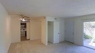 This single-floor residential unit offers a practical and comfortable layout designed for easy everyday living. The main living area is finished with wall-to-wall carpeting in a neutral beige tone, creating a warm and inviting atmosphere. A ceiling fan with a light fixture is mounted overhead, providing both ventilation and ambient lighting to the space.

The living area flows openly into the kitchen, which features dark cabinetry, a stainless steel range, and an overhead exhaust hood. A skylight or overhead light fixture in the kitchen area adds brightness to the cooking space, complementing the dark wood tones of the cabinetry.

A built-in closet with a hanging rod is conveniently positioned within the living area, offering practical storage without the need for additional furniture. The unit's front entry door is located nearby, making for a straightforward and accessible entry point.

Throughout the space, textured ceilings and neutral wall tones contribute to a clean, understated aesthetic. HVAC vents are integrated into both the ceiling and walls, ensuring year-round climate comfort. The overall design prioritizes functionality and ease of use, making this a well-appointed single-floor living space.