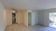 This single-floor residential unit offers a practical and comfortable layout designed for easy everyday living. The main living area is finished with wall-to-wall carpeting in a neutral beige tone, creating a warm and inviting atmosphere. A ceiling fan with a light fixture is mounted overhead, providing both ventilation and ambient lighting to the space.

The living area flows openly into the kitchen, which features dark cabinetry, a stainless steel range, and an overhead exhaust hood. A skylight or overhead light fixture in the kitchen area adds brightness to the cooking space, complementing the dark wood tones of the cabinetry.

A built-in closet with a hanging rod is conveniently positioned within the living area, offering practical storage without the need for additional furniture. The unit's front entry door is located nearby, making for a straightforward and accessible entry point.

Throughout the space, textured ceilings and neutral wall tones contribute to a clean, understated aesthetic. HVAC vents are integrated into both the ceiling and walls, ensuring year-round climate comfort. The overall design prioritizes functionality and ease of use, making this a well-appointed single-floor living space.