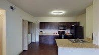 This single-floor, 2-bedroom, 1-bathroom residence offers a practical and comfortable layout designed for everyday living. The kitchen serves as a central highlight, featuring dark espresso-toned cabinetry that contrasts elegantly with granite-style countertops. Black appliances, including a range, over-the-range microwave, and refrigerator, complement the cohesive design. A peninsula with a double-basin sink adds additional prep space and contributes to an open feel, while rich dark hardwood-style flooring grounds the kitchen and adjacent areas. A dedicated in-unit laundry area is conveniently situated just off the kitchen, adding a practical touch to the floor plan. The bedrooms are carpeted for comfort and each feature ceiling fans with light fixtures and windows fitted with blinds that allow for natural light control. Closets with sliding doors and full-length hanging rods provide ample storage. The bathroom is clean and functional, equipped with a full soaking tub and shower combination surrounded by white tile, complete with a shower curtain rod. Neutral wall tones throughout the residence create a bright and inviting atmosphere, offering a versatile backdrop suited to a variety of interior styles.