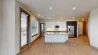 Located at 201 McKinney Village Pkwy in McKinney, Texas, this single-floor residence offers a thoughtfully designed layout with modern finishes and functional living spaces. The open-concept kitchen serves as the centerpiece of the home, featuring a large granite-topped island with an integrated sink, white upper cabinetry paired with rich dark lower cabinets, a herringbone tile backsplash, stainless steel appliances including a refrigerator and microwave, and light wood-style flooring. Large windows allow ample natural light to fill the space and provide views of the surrounding area. The bedrooms are carpeted for comfort and each includes a ceiling fan and a window with exterior views, creating bright and airy retreats. The bathroom is well-appointed with a granite-topped dark wood vanity, subway-tiled soaking tub and shower combo, wood-look flooring, and recessed lighting. A dedicated entryway features built-in shelving and a mudroom-style locker area, providing excellent organizational storage. The in-unit laundry room accommodates a full-size washer and dryer and includes overhead shelving for additional storage. Recessed lighting throughout and a neutral color palette contribute to the clean, contemporary ambiance of this well-equipped home.