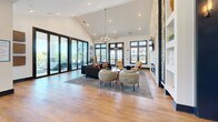 Located at 105 Sweeten Grass Hill in Asheville, NC, this single-floor space seamlessly combines a kitchen and living room into one expansive, open-plan layout. The interior is defined by soaring vaulted ceilings that amplify the sense of space and airiness, complemented by warm hardwood flooring that runs throughout.

The living area is anchored by a striking floor-to-ceiling stacked stone fireplace with built-in shelving on either side, serving as a dramatic focal point. A tasteful chandelier hangs above a curated seating arrangement of contemporary sofas and accent chairs. Expansive black-framed floor-to-ceiling sliding glass doors line an entire wall, flooding the room with natural light and providing seamless access to a covered outdoor deck with lush greenery views. Matching black-framed windows further enhance the connection between interior and exterior.

The kitchen is equally refined, featuring rich dark cabinetry, a deep granite countertop with striking veining, and stainless steel appliances including a built-in oven. A large granite-topped island with bar seating provides an ideal gathering spot, illuminated by an elegant pendant chandelier. The kitchen's warm, large-format tile backsplash adds texture and visual depth. Together, these spaces create a sophisticated, light-filled environment well-suited for both everyday living and entertaining.