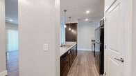 This single-floor residential unit offers a thoughtfully designed layout with modern finishes throughout. The open-concept kitchen serves as the centerpiece, showcasing rich dark-toned cabinetry, granite countertops, a peninsula with an undermount sink illuminated by stylish pendant lighting, and a full suite of stainless and black appliances. A subway tile backsplash adds a refined touch, while wood-look plank flooring extends seamlessly into the adjacent living area. The living space is bright and airy, benefiting from recessed lighting and a sliding glass door that floods the room with natural light and provides access to an outdoor area. Neutral wall tones throughout create a clean, contemporary ambiance. The bedrooms are generously proportioned, featuring soft carpeting and direct access to connecting spaces. The primary bedroom leads to a spacious walk-in closet outfitted with built-in shelving and hanging rods, offering ample storage. The bathroom is finished with marble-style porcelain tile flooring, a dark wood vanity with a white countertop, a large mirror, and polished chrome fixtures. Recessed lighting and clean white paneled doors complete the well-coordinated aesthetic across the entire unit.
