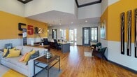 Located at 14650 Foliage Ave in Apple Valley, MN, this single-story community clubhouse offers a well-appointed and welcoming environment designed for both social gatherings and productive meetings. The space is unified by warm hardwood flooring, bold golden-yellow accent walls, and soaring ceilings that amplify the sense of openness throughout.

The kitchen is a central highlight, featuring dark cabinetry, granite countertops, stainless steel appliances, and a large island with bar-height seating for multiple guests. Pendant lighting and generous windows overlooking an outdoor pool area enhance the bright, functional atmosphere.

Adjacent to the kitchen, a formal dining area impresses with floor-to-ceiling windows, striped drapery, an elegant chandelier, and a wall-mounted flat-screen TV — ideal for group gatherings or presentations. A separate, more intimate meeting room offers a quieter setting with natural light, gold leather chairs, and curated wall art.

The lounge area serves as a social anchor, anchored by a dramatic full-height brick fireplace with a mounted TV above, plush yellow and gray seating, and a bold area rug. Large-scale abstract artwork and crown molding add refined character.

The reception and lobby area features soaring ceilings, a staffed service counter, and an open layout that sets a welcoming tone upon arrival. Together, these spaces form a cohesive, vibrant community hub.