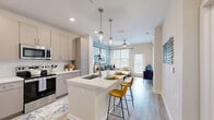 Located at 1951 Integra Dr in West Melbourne, Florida, this 1-bedroom, 1-bathroom residence offers a thoughtfully designed open-concept layout finished with light wood-style flooring throughout the main living areas. The kitchen is a standout feature, boasting taupe cabinetry, quartz countertops, stainless steel appliances — including a French door refrigerator, range, and built-in microwave — and a central island with seating for two, illuminated by stylish pendant lighting. The kitchen flows seamlessly into the living room, which is bathed in natural light from large windows and a glass door that opens to a private balcony, offering outdoor views. A ceiling fan adds comfort to the living area. The bedroom features plush carpeting, a bold accent wall, a ceiling fan, and a generous window that brings in abundant natural light. A dedicated closet provides ample storage. The bathroom features wood-look flooring, a single-sink vanity, a glass-enclosed shower, and direct access to the walk-in closet, creating a practical and cohesive private suite. The overall ambiance is modern and bright, with a clean, contemporary aesthetic throughout.