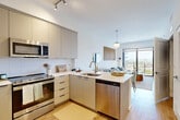 Located at 3201 N Federal Hwy in Oakland Park, Florida, this well-appointed one-bedroom, two-bathroom residence offers a thoughtfully designed open-concept layout finished with light hardwood flooring and a clean, contemporary aesthetic throughout. The kitchen is outfitted with sleek, flat-front cabinetry in a warm neutral tone, stainless steel appliances including a French-door refrigerator and built-in microwave, a peninsula with bar seating, and a crisp white countertop that flows seamlessly into the dining and living areas. The living room is bright and airy, anchored by floor-to-ceiling sliding glass doors that open to a private balcony showcasing expansive city views — a standout feature that fills the space with natural light. The bedroom is serene and spacious, featuring a large window with sweeping outdoor views, light hardwood floors, and a dedicated closet. Two bathrooms serve the unit: a full bath with a glass-enclosed walk-in shower accented by vertical tile and a floating vanity, and a second bathroom with clean, minimal finishes. Track lighting in the kitchen and pendant fixtures in the living area add modern character, while the overall palette of whites and warm neutrals creates a cohesive, inviting ambiance throughout.