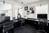 Located at 1630 Orchard Dr in Placentia, California, this single-floor leasing center is designed with a clean, contemporary aesthetic that blends functionality with modern style. The space is thoughtfully laid out to serve as a professional business hub, anchored by a long, dark-surfaced workstation that accommodates multiple computer setups, including both PC and Mac configurations, making it well-equipped for staff and prospective residents alike.

Large glass windows and frosted-panel partitions line the interior, allowing natural light to flow throughout while offering views into adjacent community areas filled with lush greenery and outdoor seating. Sleek pendant lighting in a matte black finish hangs above the workstation, adding a modern touch to the illuminated workspace.

The walls are adorned with a carefully curated selection of framed artwork, ranging from bold black-and-white graphic prints to vibrant abstract pieces and a striking large-format photograph of a vintage New York City subway car, giving the space a creative, gallery-like atmosphere. The entryway features a frosted glass door with business hours etched in, welcoming visitors with a polished first impression. Dark carpet tiles ground the space, complementing the monochromatic design palette throughout. Overall, the leasing center exudes a professional yet artistic ambiance.