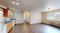 Located at 245 SE 146th Ave in Portland, Oregon, this single-floor, 2-bedroom unit offers a practical and well-organized layout. The combined kitchen and living area forms the heart of the home, with durable hardwood-style flooring that extends throughout the entire unit. The kitchen is equipped with light wood cabinetry, open shelving, granite-style countertops, a double sink, and white appliances including a refrigerator, electric range, microwave, and dishwasher — providing a fully functional cooking space. The living area is bright and open, featuring a large window with vertical blinds that allows natural light to fill the room, complemented by a wall-mounted HVAC unit for year-round comfort. A central hallway connects the main living space to the bedrooms and includes a stacked in-unit washer and dryer. The spacious primary bedroom features a walk-in closet with built-in shelving and hanging rods, offering generous storage. The second bedroom is clean and well-proportioned with neutral walls and matching flooring. Throughout the unit, the neutral color palette and clean finishes create a bright, move-in-ready atmosphere suited for everyday living.