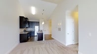 This 2-bedroom, 2-bathroom residence in Summer Phase I is designed with an open-concept floor plan that maximizes space and promotes a natural flow throughout the home. The kitchen is a standout feature, showcasing dark espresso cabinetry that contrasts beautifully with granite countertops and stainless steel appliances, including a refrigerator and range. A peninsula with a built-in sink serves as both a functional workspace and a casual dining or entertaining area, accented by stylish pendant lighting overhead. The kitchen transitions seamlessly into the main living area, which features warm neutral carpeting and bright white walls that create a clean, inviting atmosphere. Vaulted ceilings add a sense of height and openness throughout the space, enhancing the airy feel. Rich hardwood-style flooring in the kitchen and entryway areas complements the overall aesthetic. The layout includes multiple doorways leading to the bedrooms and additional living areas, offering a practical and well-organized floor plan. Natural light filters through the space, contributing to its welcoming ambiance. This residence combines modern design elements with functional living spaces, making it a comfortable and stylish home.
