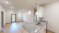 Located at 691 Union Chapel Rd in Cedar Creek, TX, this single-story 2-bedroom, 2-bathroom residence offers a clean, modern design with thoughtful finishes throughout. The open-concept kitchen and living area serves as the heart of the home, featuring white shaker-style cabinetry, granite countertops with a double undermount sink, and stainless steel appliances including a refrigerator, electric range, microwave, and dishwasher. Pendant lighting over the kitchen peninsula adds a contemporary touch, while recessed lighting illuminates the space efficiently. Light hardwood-style flooring runs through the main living areas and kitchen, contributing to a bright, cohesive aesthetic. The living area benefits from natural light courtesy of a glass exterior door and an adjacent window fitted with blinds. Both bedrooms are carpeted and offer a comfortable, quiet retreat — the primary bedroom is generously sized, while the second bedroom is well-proportioned with a ceiling fan and natural light from a window. The two bathrooms are well-appointed: one features a walk-in glass-enclosed shower with white tile surround, while the other includes a full tub-shower combo with matching white tile. Both bathrooms include granite vanities and brushed nickel fixtures. A dedicated closet and efficient entry hallway round out this well-designed residence.