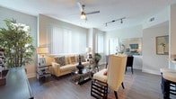 This three-floor residence is thoughtfully designed with a bright, open-concept layout that seamlessly connects the living, dining, and kitchen areas. The living room features wood-style flooring, a ceiling fan, track lighting, and large windows dressed with vertical blinds that invite generous natural light. Comfortable seating arrangements and a glass-top coffee table create an inviting atmosphere, while a staircase visible from the main level connects the floors.

The kitchen is a functional centerpiece, showcasing an expansive granite-topped island with bar seating, white cabinetry, a mosaic tile backsplash, stainless steel appliances—including a refrigerator, range, and microwave—and a deep basin sink with a modern faucet. An adjacent dining area offers an intimate space for meals.

The bedrooms are well-proportioned, featuring ceiling fans, plush carpeting or wood-style flooring, walk-in closets, and ample natural light. An in-unit laundry closet housing a full-size washer and dryer adds everyday convenience. Neutral tones and clean architectural lines throughout give the space a cohesive, modern aesthetic.