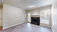 This single-floor residence offers a thoughtfully arranged layout with consistent finishes throughout. The living room serves as the centerpiece of the home, featuring a classic wood-surround fireplace with dark tile hearth, neutral-toned walls, light wood-style flooring, and multiple windows fitted with blinds that invite natural light from multiple directions. A track lighting fixture and direct access to an exterior door add both function and convenience to this central gathering space.

The galley-style kitchen is efficiently designed with white cabinetry, light countertops, stainless steel appliances including a refrigerator, range, and dishwasher, and a single-basin sink. A pass-through connects the kitchen to the adjacent dining and living areas, enhancing the open feel of the shared spaces.

A ceiling fan overhead and direct sightlines to a closet and bathroom highlight the practical flow of the secondary living area. The bedrooms are quiet, well-proportioned rooms with the same light wood-style flooring, neutral walls, textured ceilings, and windows providing natural light. The bathroom features a full tub and shower combination with white tile surround and chrome fixtures, maintaining the clean, understated aesthetic found throughout the home.