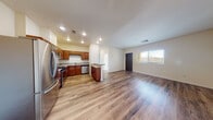 This single-story residence at 2100 N 10th St in El Centro, California offers a well-designed, functional layout with a clean, modern aesthetic throughout. The heart of the home is an open-concept living and kitchen area, where warm wood-look flooring extends seamlessly across the space, creating a bright and cohesive feel. The kitchen is outfitted with rich cherry-toned cabinetry, granite-style countertops, and a full suite of stainless steel appliances including a refrigerator, gas range, and dishwasher. A peninsula provides additional counter space and further defines the transition between the kitchen and the generously sized living area, which receives natural light through a window fitted with blinds. The bedrooms feature plush carpeting and ceiling fans, with windows that invite natural light. The primary bedroom includes a dedicated walk-in closet and direct access to a private bathroom. An additional bathroom features a tub-shower combination, wood-look flooring, a vanity with granite-style countertops, and rich cabinetry consistent with the home's overall design language. The layout is practical and well-proportioned, making efficient use of every area while maintaining a comfortable and inviting atmosphere throughout.