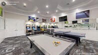 This billiards and game room in Durham, NC, is a dedicated entertainment space thoughtfully designed to accommodate a wide variety of recreational activities. The room's architecture is defined by an elegant tray ceiling with crown molding and recessed lighting, lending a polished, upscale character to what is fundamentally a lively social environment. The textured, multi-toned carpet adds visual depth underfoot while providing a durable surface suited to high activity.

At the heart of the space, a full-size pool table serves as the central focal point, complemented by a second pool table nearby, offering ample room for simultaneous gameplay. A regulation ping-pong table and a foosball table round out the core gaming options. Along one wall, a lineup of classic arcade and pinball machines adds a retro entertainment dimension, while a high-top table with bar stools provides a comfortable spot for spectators or casual gathering.

A large mirrored wall runs along one side of the room, visually expanding the space and reflecting the vibrant energy within. Multiple wall-mounted flat-screen televisions are strategically positioned throughout, ensuring visibility from virtually every corner. Bold billiards-themed artwork adorns the walls, reinforcing the room's spirited theme and completing its dynamic, inviting ambiance.