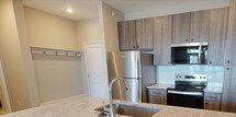 This 690-square-foot, one-bedroom, one-bathroom apartment at Unit 1501, 80 Lawrenceville Suwanee Rd, Lawrenceville, GA 30044, offers a thoughtfully designed single-floor layout. The open-concept kitchen and living area features light wood-style flooring, recessed lighting, and a ceiling fan. The kitchen is equipped with stainless steel appliances including a refrigerator, electric range, and built-in microwave, complemented by dark wood-tone cabinetry, a subway tile backsplash, and a granite-topped island with an undermount sink. The living area receives ample natural light through large windows and a glass-panel door offering outdoor views. The 160-square-foot primary bedroom is carpeted, includes a ceiling fan, and features two windows with exterior views. It connects to a dedicated closet outfitted with wire shelving and carpet flooring. The bathroom includes a wood-tone vanity with granite countertop, a glass-enclosed shower, tile flooring, and a separate toilet area. A hallway connects all rooms, completing this efficiently planned residential unit.