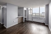 Located on the 9th floor at 245 Main St in Toronto, this two-bedroom, one-bathroom unit offers a practical and modern layout across a single level. The living area is bright and open, featuring warm wood-look laminate flooring and soft grey walls that create a clean, neutral palette throughout. Large windows allow abundant natural light to filter in while framing elevated views of the surrounding Toronto cityscape and neighbourhood below.

The kitchen is thoughtfully designed with contemporary two-tone cabinetry, white quartz countertops, and stainless steel appliances including a full-size refrigerator, electric cooktop, built-in microwave, and dishwasher — offering a functional and stylish space for cooking.

The primary bedroom is generously proportioned, with mirrored sliding closet doors that enhance the sense of space. The second bedroom is equally well-sized and features a baseboard heating unit along the exterior wall. Both rooms continue the consistent laminate flooring and neutral tones found throughout the unit.

The bathroom is finished in a clean, modern style with white subway tile surrounding the bathtub, a wood-grain vanity with quartz countertop, and a large mirror above. Roller blinds are present on windows throughout, adding privacy and light control. The overall ambiance is contemporary, calm, and move-in ready.