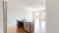 Located at 540 New Park Ave in West Hartford, CT, this single-floor residence offers a thoughtfully designed open-concept layout filled with natural light and contemporary finishes. The living area is spacious and inviting, featuring warm hardwood flooring that extends throughout the unit and crisp white walls that create a bright, airy atmosphere. Large windows and a glass door leading to an outdoor area allow abundant sunlight to pour in, offering views of a private fenced exterior space.

The kitchen serves as a central hub of the home, anchored by a generous island with a granite countertop, an integrated sink, and a stainless steel dishwasher. Complementing the island, the kitchen features gray cabinetry, matching granite counters along the back wall, and a full suite of stainless steel appliances including a refrigerator, gas range, and microwave.

The bedroom is a well-proportioned, light-filled room with hardwood floors and a window overlooking the outdoors. The bathroom is cleanly appointed with large-format tile flooring, a floating granite-topped vanity with dark wood cabinetry, a wall-mounted mirror, and accessibility-friendly grab bars, reflecting a thoughtful and inclusive design approach throughout the home.