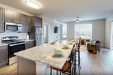 This well-appointed 2-bedroom, 2-bathroom residence in Madison, Wisconsin offers a thoughtfully designed open-concept layout across a single floor. The entry opens directly into a bright, flowing living space where the kitchen, dining area, and living room seamlessly connect. The kitchen is a standout, featuring dark espresso cabinetry, a large granite-topped island with bar seating, stainless steel appliances including a refrigerator, range, and dishwasher, and a classic white subway tile backsplash. Pendant and flush-mount lighting complement the space throughout. The dining and living areas benefit from large windows that invite abundant natural light and views of the surrounding neighborhood, while light-toned hardwood-style flooring unifies the entire open plan. The primary bedroom is a comfortable retreat with a window overlooking the outdoors, and both bedrooms are supported by dedicated closet space. The bathrooms are finished with granite-topped dark vanities and walk-in glass-enclosed showers. Additional conveniences include in-unit laundry and four closets for ample storage. The overall ambiance is clean, modern, and welcoming throughout.