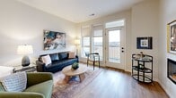 This thoughtfully designed one-bedroom, one-bathroom residence offers a highly functional open-concept layout finished with contemporary details throughout. The kitchen serves as a central hub of the living space, featuring gray shaker-style cabinetry, white quartz countertops, a white tile backsplash, and stainless steel appliances. A large kitchen island with an undermount sink and bar seating provides additional workspace and casual dining, illuminated by two pendant lights overhead. Light hardwood-style flooring flows through the kitchen and living areas, enhancing the bright, airy feel of the space.

The living room is anchored by a wall-mounted electric fireplace and opens directly to a private balcony through glass-paneled doors with transom windows, inviting abundant natural light and outdoor views. The bedroom is generously proportioned, featuring plush carpet, dual windows with scenic views, and direct access to a dedicated closet with built-in shelving and hanging storage. The full bathroom includes a single vanity with white countertops, a lighted mirror, and a combination tub and shower. A in-unit laundry closet with side-by-side washer and dryer and overhead shelving completes this efficient, modern residence.