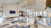 Located at 5 Ledge Dr in Schenectady, NY, this single-floor space offers a thoughtfully designed open-concept layout combining a kitchen and living area. The architecture is defined by dramatic vaulted ceilings that rise to impressive heights, creating a sense of grandeur and openness throughout. Exposed industrial ductwork adds a contemporary edge to the design.

The living area is anchored by an eye-catching geometric patterned floor featuring a blend of blue, gray, and neutral tones. Floor-to-ceiling windows line the walls, flooding the interior with abundant natural light while providing views of the surrounding neighborhood. A sliding glass door offers direct access to an outdoor patio area. Recessed lighting and wall-mounted sconces complement the natural light throughout.

The kitchen features white cabinetry, dark countertops, stainless steel appliances, and a large central island with an undermount sink. A textured accent wall adds warmth and visual interest. The open flow between the kitchen and living space makes the layout highly functional. Overall, the space presents a clean, modern aesthetic with a sophisticated and welcoming ambiance.