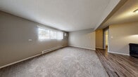 Located at 2704 Westmar Ct in Toledo, Ohio, this one-bedroom, one-bathroom unit offers a practical and well-organized single-floor layout. The combined kitchen and living area forms the heart of the space, with the kitchen featuring gray cabinetry, a double-basin sink, laminate countertops, and black appliances including a range and full-size refrigerator. Durable wood-look vinyl plank flooring runs throughout the kitchen area, transitioning into plush carpeting in the living and bedroom spaces. The living room receives natural light through a large window fitted with vertical blinds, and is equipped with a wall-mounted air conditioning unit and baseboard heating. Neutral taupe-toned walls and a textured ceiling carry throughout, creating a cohesive and understated aesthetic. The bedroom is a comfortable size, offering a full-panel closet with louvered doors for ample storage, a window for natural light, and continued baseboard heating. Three closets total provide generous storage across the unit. The bathroom is clean and functional, featuring a tub/shower combo, a single-sink vanity with white cabinetry, and wood-look vinyl flooring. Baseboard heating is present here as well, ensuring consistent warmth throughout the entire unit.