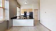 Located at 46 4th Street East in the heart of downtown Saint Paul, Minnesota, this one-bedroom, one-bathroom unit offers a thoughtfully organized single-floor layout. The combined kitchen and living area serves as the central hub of the space, characterized by terrazzo flooring that runs throughout and lends a clean, durable aesthetic. The kitchen is well-appointed with light maple cabinetry, dark granite countertops, a peninsula with a built-in sink, and black appliances including a gas range and refrigerator. A wall of windows fitted with wood-trimmed blinds fills the kitchen with natural light and frames views of the surrounding downtown Saint Paul streetscape. The living area flows naturally from the kitchen, providing an open and functional layout. The bedroom is a well-proportioned, quiet retreat with two windows offering additional urban views, terrazzo flooring, and a neutral color palette that creates a calm atmosphere. Two closets provide practical storage throughout the unit. The bathroom features a full tub-shower combination, terrazzo flooring, a light maple vanity with a dark granite countertop, and clean, minimal finishes. A hallway connects the rooms with ease. Wall sconce lighting adds a warm, modern touch to the interior. This unit combines urban convenience with clean, contemporary design elements throughout.