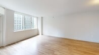 Located on the 9th floor at 1221–1331 S Eads St in Arlington, VA, this 2-bedroom, 1-bathroom residence offers a clean, modern aesthetic throughout. Light wood-tone flooring runs continuously across all rooms, complementing the bright white walls and creating a cohesive, airy feel.

The kitchen is a standout feature, outfitted with white shaker cabinetry, white quartz countertops, a peninsula with a undermount sink and matte black pull-down faucet, and a full suite of stainless steel appliances including a gas range, built-in microwave, and refrigerator. Recessed lighting keeps the space well-lit and functional.

The open living area benefits from large windows that flood the room with natural light and frame views of the surrounding Arlington cityscape. A glass door leads to a private balcony, extending the living space outdoors.

The generously sized primary bedroom features expansive windows with sweeping city views, while the second bedroom also enjoys ample natural light through its own large window. Both rooms offer a calm, neutral palette ideal for comfortable living.

The bathroom is finished with white subway tile in the tub/shower surround, accented by elegant brushed gold fixtures including the showerhead, faucet, and curtain rod hardware — adding a refined touch to the space.