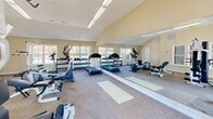 Located at 414 Berckmans Rd in Augusta, Georgia, this dedicated fitness center is housed in a single-story structure designed to support a comprehensive workout experience. The room features vaulted ceilings that lend a sense of openness and airiness, enhancing the overall atmosphere for exercise. Warm, neutral-toned walls paired with carpeted flooring create a comfortable and functional environment throughout the space.

Natural light flows in generously through multiple large windows positioned along the perimeter walls, offering views of the surrounding outdoor area and keeping the space feeling bright and inviting. Overhead fluorescent lighting supplements illumination for evening or low-light use.

The fitness center is outfitted with a well-rounded selection of equipment, including multiple treadmills, elliptical cross-trainers, and a stationary bike for cardiovascular workouts. A multi-station cable machine and an adjustable weight bench cater to strength training needs, while a tiered dumbbell rack stocked with a range of free weights provides versatile resistance options. Yoga mats on the floor support stretching and floor exercises.

A full-length wall mirror runs along one side of the room, visually expanding the space and allowing users to monitor their form during workouts. The layout is thoughtfully organized to allow comfortable movement between equipment stations, making this fitness center a practical and well-appointed facility.