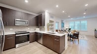 This single-floor residence showcases a cohesive contemporary design with light hardwood-style flooring and crisp white walls flowing throughout. The kitchen is a standout feature, equipped with dark espresso cabinetry, stainless steel appliances, a neutral tile backsplash, and a central island with a white quartz countertop, undermount sink, and bar seating — ideal for both cooking and casual dining. The open layout connects the kitchen seamlessly to a dedicated dining area, which benefits from recessed lighting and built-in shelving along one wall, adding functional display space.

The living room is bright and welcoming, with large windows fitted with horizontal blinds that allow abundant natural light while maintaining privacy. The bedrooms continue the light, airy aesthetic, each featuring generous windows, ceiling fans, and ample room for furnishings. The bathroom is finished with large-format tile flooring, dark wood cabinetry, a white quartz vanity, and a well-lit mirror — with an adjacent walk-in closet space providing practical storage. Throughout the residence, recessed lighting and clean-lined architectural details contribute to a polished, modern ambiance.