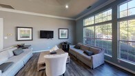 Located at 100 Northcreek Dr in Durham, NC, this single-floor space offers a thoughtfully designed open layout that balances comfort and functionality. The main living area is generously sized, featuring rich dark hardwood-style flooring, crown molding, and recessed lighting throughout. Large multi-pane windows flood the room with natural light while offering pleasant views of the surrounding greenery, and a ceiling fan adds a practical touch to the airy atmosphere. The kitchen is open and well-appointed, showcasing dark espresso cabinetry, granite-style countertops, a double-basin sink, and a full suite of stainless steel appliances including a refrigerator, range, and built-in microwave. A wraparound breakfast bar connects the kitchen seamlessly to the living space, ideal for casual dining or entertaining. Adjacent to the kitchen, a tile-surround fireplace with a classic white mantle serves as an elegant focal point. A dedicated dining area is bathed in abundant natural light courtesy of expansive floor-to-ceiling windows on multiple walls, creating a bright and inviting atmosphere with outdoor views of the surrounding landscape. Crown molding and consistent neutral tones carry throughout, lending the space a cohesive and polished character overall.
