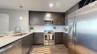 Located at 401 S. Graham Street in Charlotte, NC, this contemporary one-bedroom, one-bathroom residence offers a well-appointed layout across a single floor. The open-concept design connects the kitchen, dining, and living areas, maximizing the functional use of space throughout.

The kitchen is outfitted with dark, textured cabinetry that extends to the ceiling, white quartz countertops with subtle veining, a subway tile backsplash, and a full suite of stainless steel appliances, including a gas range, over-the-range microwave, dishwasher, and side-by-side refrigerator. A peninsula with pendant lighting above provides additional workspace and casual seating potential, seamlessly connecting to the living area.

The living room is anchored by floor-to-ceiling windows that frame panoramic views of the Charlotte skyline, flooding the space with abundant natural light and creating a striking visual focal point. Wood-style flooring runs throughout.

The generously sized primary bedroom continues the floor-to-ceiling window theme, offering the same impressive city views and a ceiling fan. A teal accent wall adds a bold design element to the room.

The bathroom features a glass-enclosed walk-in shower with white subway tile surround, and connects directly to a dedicated walk-in closet with built-in shelving and hanging rods.