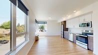 This well-designed 2-bedroom, 1-bathroom unit offers a thoughtfully laid-out single-floor plan that maximizes functionality and comfort. The open-concept living and kitchen area serves as the heart of the space, bathed in natural light from expansive windows that frame views of surrounding greenery and the neighborhood. Light hardwood-style flooring runs throughout, lending warmth and visual continuity to every room.

The kitchen is outfitted with a full suite of stainless steel appliances — including a refrigerator, electric range, microwave, and dishwasher — complemented by a two-tone cabinetry design featuring white upper cabinets and wood-finish lower cabinets. Recessed lighting overhead adds a clean, modern touch.

Both bedrooms are bright and well-proportioned, each featuring windows that invite natural light and closet storage. The primary bedroom includes a built-in closet with wire shelving, while the second bedroom offers its own dedicated closet. A wall-mounted HVAC unit ensures year-round climate comfort in the bedrooms.

The full bathroom is clean and modern, showcasing wood-finish cabinetry, a quartz-style countertop, a large vanity mirror, and a shower-tub combination. A narrow hallway with recessed lighting connects the living areas to the private quarters, maintaining a clear separation between spaces. The unit presents a fresh, move-in-ready aesthetic throughout.