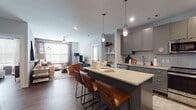 This thoughtfully designed single-floor residence offers a seamless blend of modern aesthetics and functional living. The open-concept layout connects the kitchen and living area, creating an inviting, communal atmosphere. The kitchen is a standout feature, outfitted with gray flat-panel cabinetry extending to the ceiling, white subway tile backsplash, stainless steel appliances including a refrigerator, range, microwave, and dishwasher, and a large center island with a light quartz countertop and seating for multiple bar stools, illuminated by pendant lighting. The living area is warm and stylish, featuring wood-look flooring, a ceiling fan, natural light from large windows with blinds, and curated wall art and shelving. The bedrooms are generously sized, each with rich hardwood-style floors, ample natural light, and well-considered design details. One bedroom features a bold dark accent wall paired with a large window and wood dresser, while another showcases a neutral palette with a statement diptych artwork above the bed. The bathrooms are cleanly finished with gray vanities, quartz countertops, white tile flooring, and subway-tiled tub surrounds. One bathroom features a rich teal accent wall, adding a vibrant pop of color. A built-in desk nook provides a dedicated workspace within the unit.