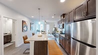 This single-floor residence features a well-designed open-concept layout that seamlessly connects the kitchen, dining, and living areas. The kitchen is a standout, equipped with rich dark-toned shaker-style cabinetry extending to the ceiling, light granite countertops, a white subway tile backsplash, and a full suite of stainless steel appliances including a refrigerator, electric range, built-in microwave, and wine cooler. A central island with pendant lighting above provides additional prep space and casual seating. Wood-look flooring runs throughout the main living areas, complementing the neutral color palette.

The living room is bright and welcoming, featuring a ceiling fan, large windows with blinds, and a glass door that introduces natural light. The bedroom offers plush carpeting, a reach-in closet, and direct sightlines to the kitchen. Two bathrooms serve the space: one features a walk-in shower with a granite-topped dark vanity, while the second includes a full tub-shower combination, a single-sink vanity with granite countertops, and wood-look flooring. Throughout, recessed lighting, clean white walls, and consistent finishes create a cohesive, modern ambiance.