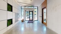 Located at 14 E Canal St in Richmond, Virginia, this single-floor space presents a thoughtfully designed lobby and amenity suite that blends contemporary aesthetics with functional comfort. The entrance foyer makes an immediate impression with its expansive floor-to-ceiling glass frontage, polished concrete floors that reflect natural light, and a striking geometric pendant light fixture overhead. A built-in mailbox wall and secure entry doors contribute to the lobby's practical layout.

Adjacent to the entrance, a warmly appointed corridor features floor-to-ceiling wood panel cladding and a built-in cushioned bench, offering a welcoming transition through the space. The corridor leads to a pair of distinct amenity rooms. The first is a stylish lounge furnished with cream upholstered seating, sculptural wood-contour coffee tables, and accent mirrors arranged against bold circle-patterned wallcovering, creating an inviting social atmosphere. The second area functions as a co-working and study space, anchored by open wood shelving units displaying books and décor, alongside dedicated desk stations and comfortable seating. Together, these rooms provide residents with versatile spaces for relaxation, socializing, and productivity in a refined, modern setting.