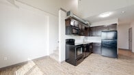 Located at 429 W Central Ave in Wichita, Kansas, this unit showcases a thoughtfully designed interior that blends industrial character with modern finishes. The open-concept main level is anchored by a well-appointed kitchen featuring rich dark espresso cabinetry, granite countertops, a white subway tile backsplash, and a full suite of black appliances including an electric range, built-in microwave, dishwasher, and refrigerator. Exposed ductwork running above the kitchen adds an urban, loft-inspired aesthetic, while soaring ceilings amplify the sense of openness throughout the main living area. Light wood-look flooring extends across the main level, contributing to a clean and contemporary feel. A carpeted staircase leads to the upper level, where a cozy loft-style space with sloped ceilings and plush carpet offers flexible use as a sleeping area, office, or additional living space. A separate room on the main level features light wood flooring, neutral walls, and a window with blinds that allows natural light to filter in. The bathroom includes a glass-panel shower enclosure with chrome hardware. The overall ambiance is modern and functional, with industrial touches that give the space a distinctive urban character.
