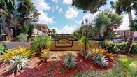 Hawaiian Palms is a rental community that makes a striking first impression with its beautifully landscaped entrance. The community sign at 3540 is framed by an abundance of tropical greenery, including towering palm trees, richly colored bromeliads, agave plants, and a variety of lush foliage that evokes a distinctly tropical ambiance. The warm-toned exterior of the multi-story residential buildings is visible beyond the entrance, complementing the vibrant reds and greens of the surrounding plantings set against red mulched garden beds. The overall aesthetic of the community reflects a Florida-inspired design, blending natural landscaping with residential architecture under open, sunny skies. The single-floor unit within the community offers a functional residential layout. While interior lighting in the available imagery is limited, the unit is situated within a well-maintained community environment that emphasizes outdoor charm and tropical character. The combination of mature trees, ornamental plants, and thoughtfully designed common areas gives Hawaiian Palms a welcoming, resort-like atmosphere that distinguishes it as an inviting place to call home.
