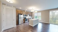 This thoughtfully designed one-bedroom, one-bathroom residence offers a efficient and functional single-floor layout. The open-concept kitchen and living area serves as the heart of the home, finished with rich hardwood-style flooring and neutral tones throughout. The kitchen is well-equipped with a full suite of stainless steel appliances, including a refrigerator, electric range, microwave, and dishwasher. Warm-toned shaker-style cabinetry provides generous storage, while a white quartz center island offers additional prep space and casual seating. Recessed lighting and pendant drum fixtures illuminate the space, and a large window invites natural light with views of the surrounding greenery.

The living area features hardwood-style flooring and a ceiling fan, with vertical blinds along a wide window wall that allows ample daylight. The bedroom is carpeted for comfort, complete with a ceiling fan, a roller shade window, and direct access to a dedicated walk-in closet outfitted with wire shelving and hanging rods for organized storage. The full bathroom includes a tub-shower combination with white subway tile surround, wood-toned vanity, and a framed mirror. Clean, contemporary finishes are carried consistently throughout the entire residence.