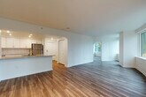 Located at 700 Virginia St in the heart of Seattle, WA, this one-bedroom, two-bathroom apartment offers a well-designed layout across a single floor. The open-concept living, dining, and kitchen area creates a spacious, connected feel, anchored by warm hardwood-style flooring throughout. Large, curved windows in the living area flood the space with natural light and frame dynamic views of Seattle's urban skyline.

The kitchen is outfitted with crisp white shaker cabinetry, granite countertops, a subway tile backsplash, and a full suite of stainless steel appliances including a refrigerator, range, microwave, and dishwasher. A peninsula provides additional prep space and casual dining.

The bedroom features track lighting, a large window with city views, and direct access to a full bathroom complete with a tiled tub/shower surround, granite vanity, and marble-style tile flooring. A second bathroom off the main living area mirrors the same clean, modern finishes. Four closets throughout the unit provide generous storage. The entrance leads smoothly into the main living spaces, enhancing the overall flow. Neutral tones, recessed lighting, and contemporary finishes give the entire unit a bright, polished ambiance.