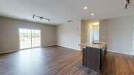 Located at 24015 Crab Apple Ct in Georgetown, Delaware, this single-floor home offers a well-designed open-concept layout that seamlessly connects the living and kitchen areas. Rich, dark hardwood-style flooring flows throughout the main living space, complemented by neutral taupe walls and recessed and track lighting overhead. The kitchen is equipped with dark espresso cabinetry, granite countertops, black appliances including a refrigerator, range, and microwave, and a central island with a sink — ideal for both cooking and casual entertaining. Sliding glass doors in the living area provide access to the outdoors and allow natural light to fill the space. The bedrooms feature plush wall-to-wall carpeting and large windows that offer views of the surrounding greenery, creating bright and comfortable retreats. The primary bedroom includes access to a dedicated en-suite bathroom and a walk-in closet. Bathrooms are finished with dark wood vanities and wood-style flooring; one features a soaking tub and shower combination, while another offers a standalone walk-in shower. The overall design is clean and consistent, with neutral tones and practical finishes that provide a move-in-ready living environment.