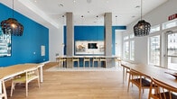 Located at 1700 CR-50 in Bay Shore, NY, this thoughtfully designed single-floor space seamlessly integrates a kitchen, dining room, and living area into one cohesive, open-plan layout. The interior is defined by a striking palette of bold cobalt blue accent walls contrasted against crisp white ceilings and light oak hardwood flooring, creating a vibrant yet welcoming atmosphere throughout.

The kitchen is a standout feature, showcasing slate-blue shaker-style cabinetry topped with clean white quartz countertops, a classic white subway tile backsplash, and open wooden floating shelves styled with coastal-themed décor. A spacious central island with bar seating and elegant pendant lighting serves as both a functional workspace and a social gathering point.

The dining area is anchored by a generous wooden communal table surrounded by Scandinavian-inspired chairs, illuminated by dramatic woven pendant lights. The bold blue feature wall, adorned with framed artwork, adds depth and character to the space.

The living area benefits from tall ceilings and large glass-paned doors and transom windows that flood the interior with natural light while offering views of the outdoor surroundings. A glass-panel entry door adds an architectural touch, enhancing the open and airy feel of this well-appointed space.
