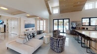 Located at 4550 Atrium Ct in Wilmington, North Carolina, this outdoor amenity space is thoughtfully designed to deliver a resort-like experience. At its centerpiece is a generously sized swimming pool with smooth, curved edges and crystal-clear blue water, complemented by a connected circular spa or wading area. The surrounding pool deck is finished in light-toned concrete, providing a clean, modern aesthetic that reflects the coastal Carolina setting.

Flanking the pool are multiple pergola-covered lounge areas supported by crisp white columns, offering shaded retreats for relaxation. Beneath the pergolas, comfortable seating options include plush daybed-style loungers with gray cushions and sleek white chaise lounges with wood-accented frames, all arranged alongside strips of manicured synthetic turf and stepping stone pathways. Natural river rock detailing at the base of privacy structures adds a refined, organic touch.

Warm, richly grained horizontal wood slat panels serve as privacy screens, creating intimate nooks within the broader communal space. These screens provide visual contrast against the white architectural elements of the surrounding buildings, which feature coastal-inspired shingle and board-and-batten siding with metal roofing. Mature trees and ornamental grasses enhance the natural ambiance, making this a well-appointed outdoor destination.