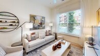 Located at 2031 Maywill St in Richmond, Virginia's Scott's Addition neighborhood, this single-floor residence showcases a thoughtfully designed contemporary interior with clean lines and a cohesive, neutral color palette throughout. The living area is bright and welcoming, featuring soaring ceilings, large windows dressed with sheer curtains and blinds, and views of the surrounding urban greenery. The space flows naturally into a well-equipped kitchen, which stands out with bold navy-blue shaker-style cabinetry extending to the ceiling, white subway tile backsplash, light countertops, and a full suite of stainless steel appliances including a refrigerator, range, microwave, and dishwasher. Light wood-tone flooring runs consistently throughout the unit, enhancing the sense of openness. The bedroom is a serene retreat with generous natural light streaming through a large window and ample room for furnishings. The bathroom is finished with light tile flooring, a clean white vanity with under-mount sink, and direct access to a walk-in closet with built-in shelving and hanging storage. A dedicated laundry area with an in-unit washer and dryer adds everyday convenience. The overall ambiance is modern, clean, and functional, reflecting a high standard of contemporary urban living.
