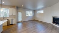 Located at 4505 Hunt St NW in Gig Harbor, Washington, this two-floor residence offers a well-designed layout with clean, contemporary finishes throughout. The main level features warm hardwood-style flooring that flows seamlessly through the open living and dining area, which is filled with natural light from multiple windows fitted with slatted blinds. A sliding glass door provides access to the outdoors, enhancing the sense of openness. The kitchen is a standout feature, boasting white shaker-style cabinetry, light quartz countertops, a subway tile backsplash, stainless steel appliances including a refrigerator, range, microwave, and dishwasher, and a central island with pendant lighting overhead. A dedicated staircase with carpet treads and a clean white handrail leads to the upper floor, where plush carpeted bedrooms offer comfortable retreats. One bedroom includes a sliding glass door opening to a private balcony with views of tall surrounding trees. The bathrooms are tastefully finished, featuring wood-toned vanities with white quartz countertops; one includes a glass-enclosed walk-in shower, another a full tub-shower combo, and a third a corner glass shower stall. The overall aesthetic is modern and move-in ready, with a neutral palette throughout.