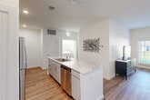 This well-appointed 2-bedroom, 1-bathroom single-floor residence offers a thoughtfully designed layout that maximizes comfort and functionality. The open-concept kitchen serves as the heart of the home, featuring sleek grey cabinetry, marble-look quartz countertops, a subway tile backsplash, and a full suite of stainless steel appliances including a refrigerator, range, and microwave. A central island with a double sink adds both prep space and visual appeal. Wood-look flooring flows throughout the main living areas, creating a warm, cohesive aesthetic. The bright and airy living room benefits from large windows that frame outdoor green views, offering an inviting space for relaxing or entertaining. A dedicated dining area sits adjacent to the living room, enhancing the open feel. A carpeted hallway connects the bedrooms, providing a quiet retreat from the main living areas. The primary bedroom is a comfortable size, featuring a window with outdoor views and plush carpet underfoot. The shared bathroom is clean and modern, finished with a marble-look vanity countertop, grey cabinetry, and wood-look flooring. An in-unit laundry area is also conveniently accessible. Throughout the space, crisp white walls and contemporary finishes contribute to a fresh, move-in-ready atmosphere.